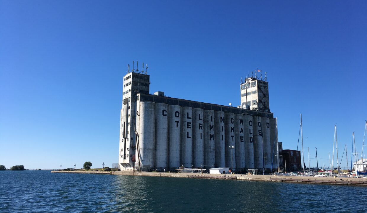 Industrial concrete silo/terminal by the water with antennas on top and the words Collingwood Terminals Limited visible against a clear blue sky.